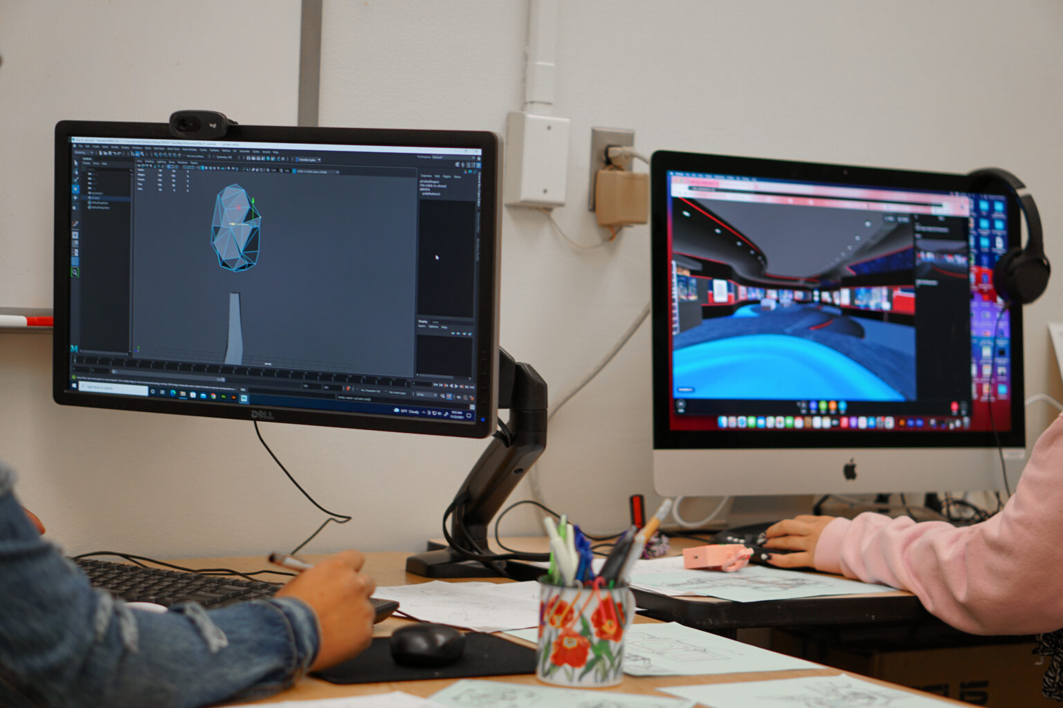 photograph of two monitors and two persons arms in view working on the VR virtual campus