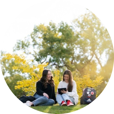 two students working on a tablet together outside of campus building on the grass.