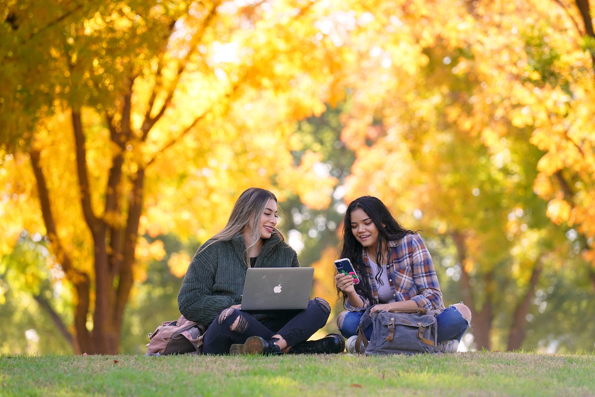 two students looking at phone and laptop